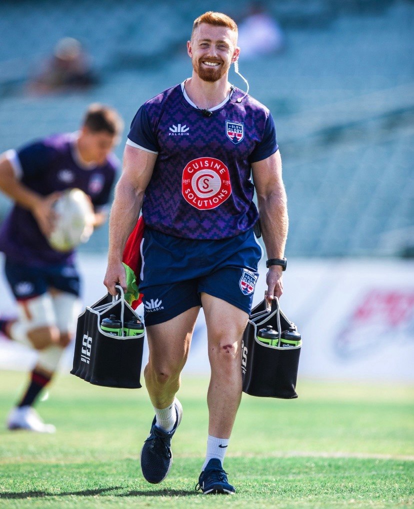 Mathew Skyner smiling while carrying rugby training equipment