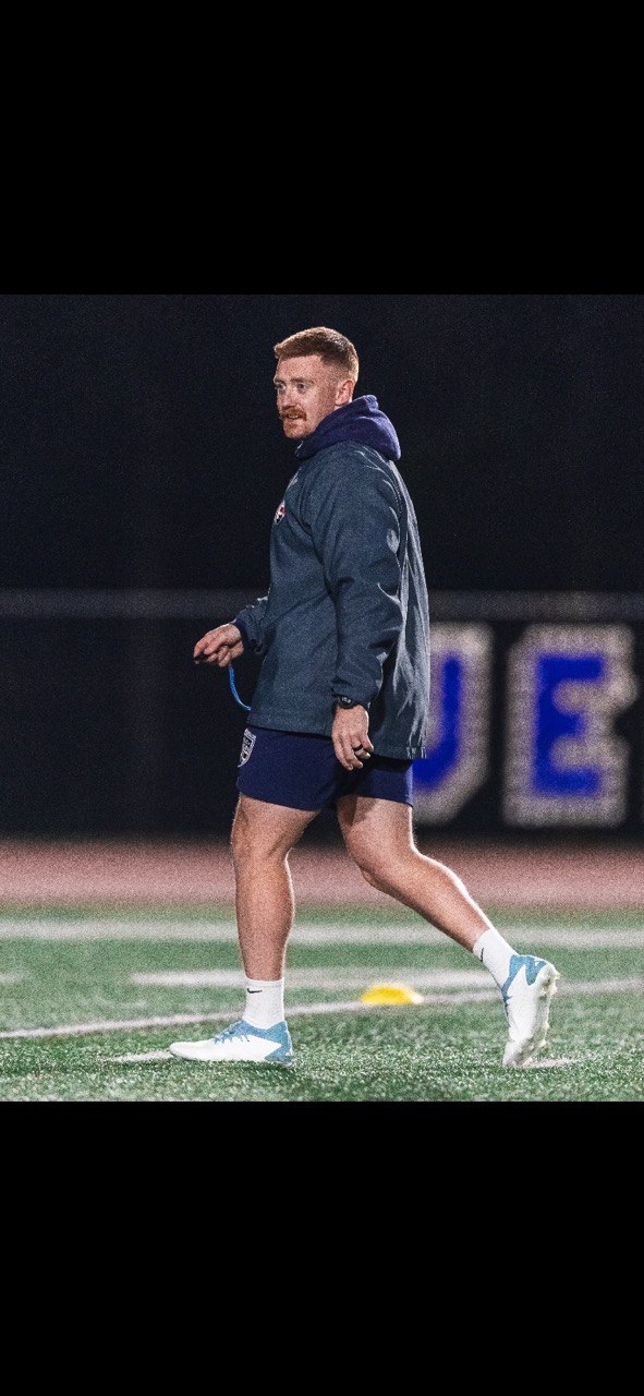 Mathew Skyner walking in profile across a floodlit rugby field at night